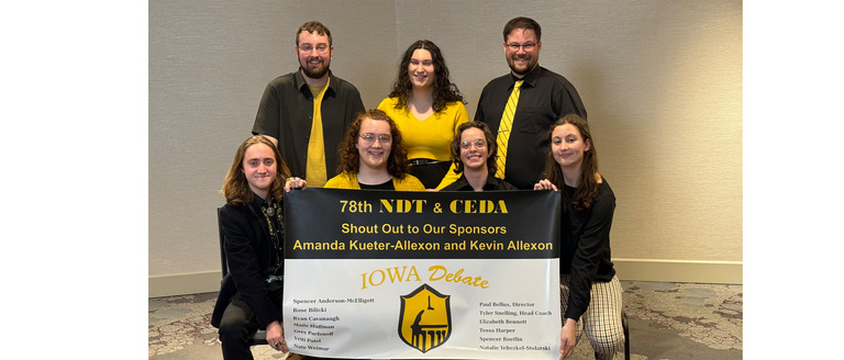 A group of people sittign and standing wearing yellow and black smiling while holding a banner