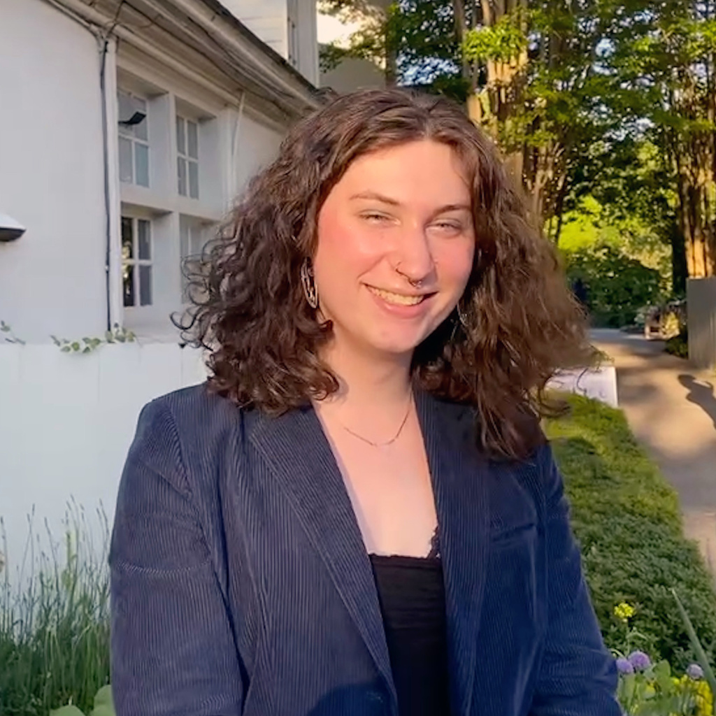 A white women with short curly brown hair standing outside and smiling