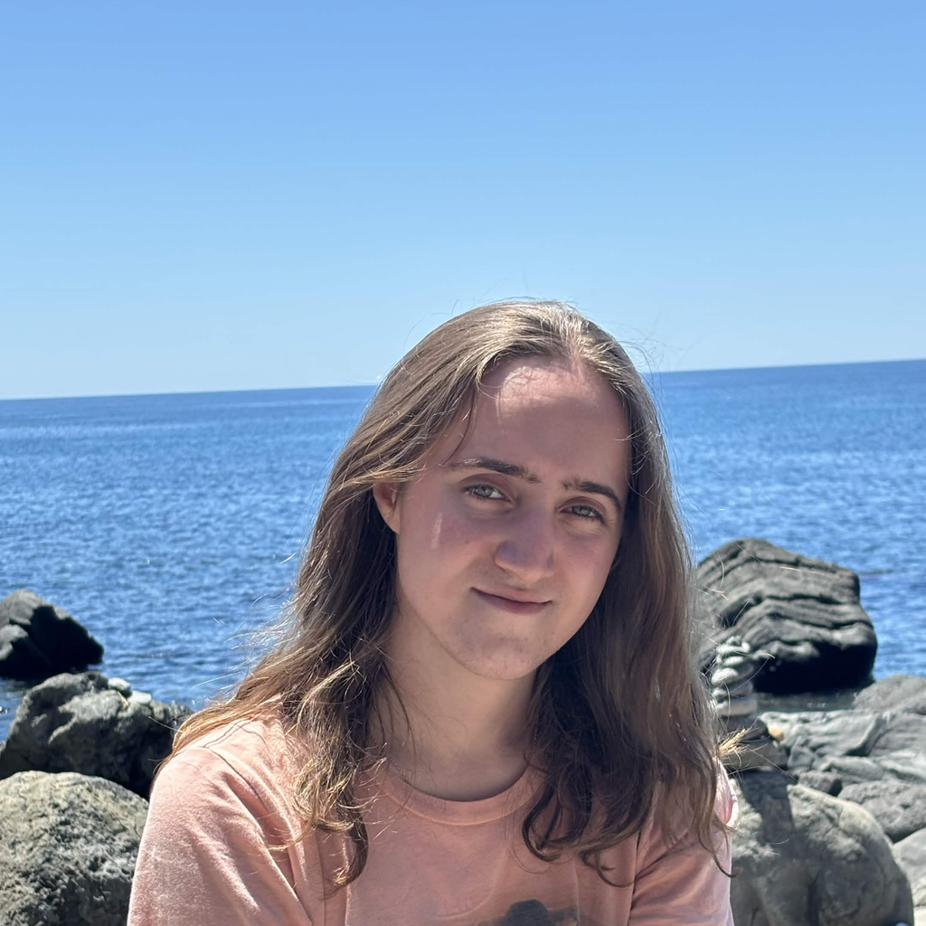 A white women sitting on rocks in front of a lake smiling 