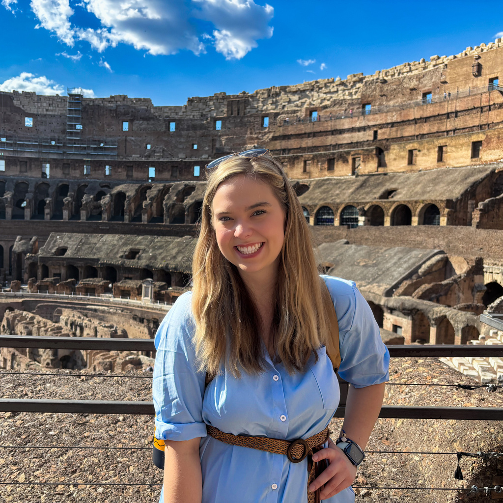 A white women smiling in front of the colosseum