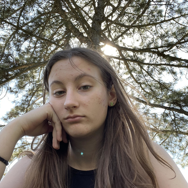 A white women with shoulder length brown hair with a tree in the background 