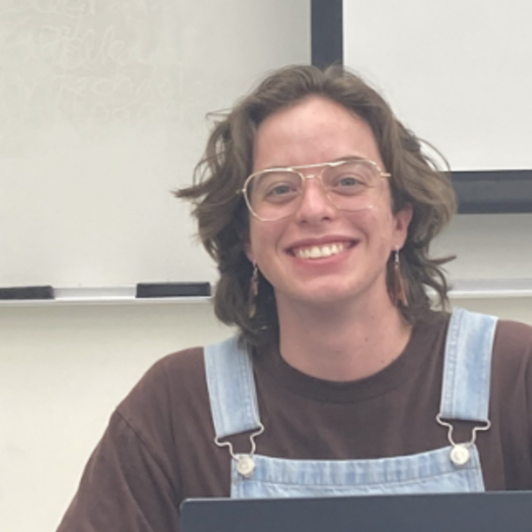 A white man with brown hair and clear glasses smiling.